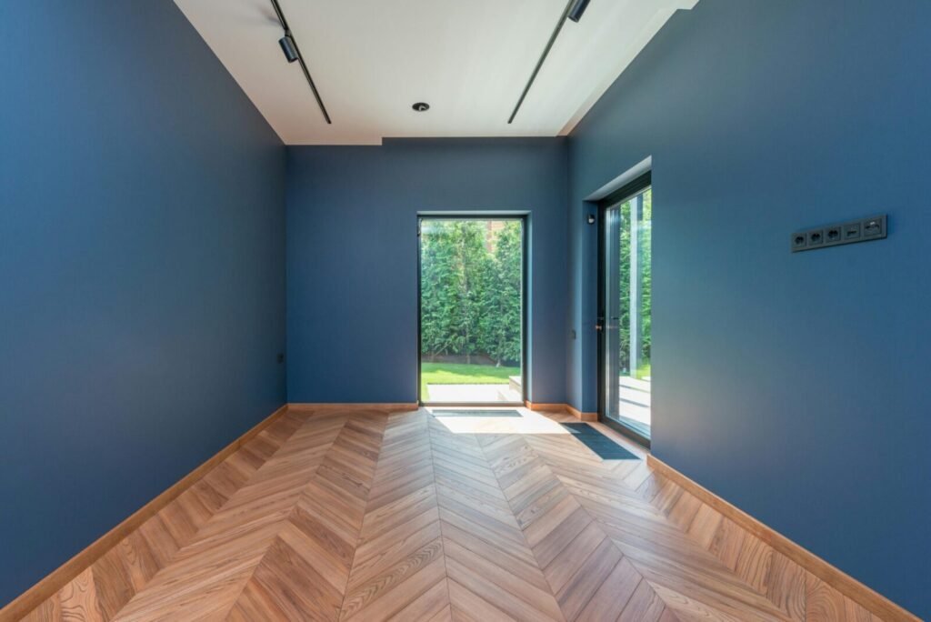 Spacious room featuring blue walls, wooden herringbone floor, and glass doors leading to a garden.